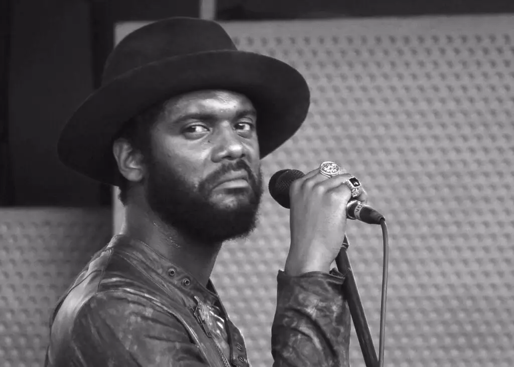 Man with hat and beard holding a mic