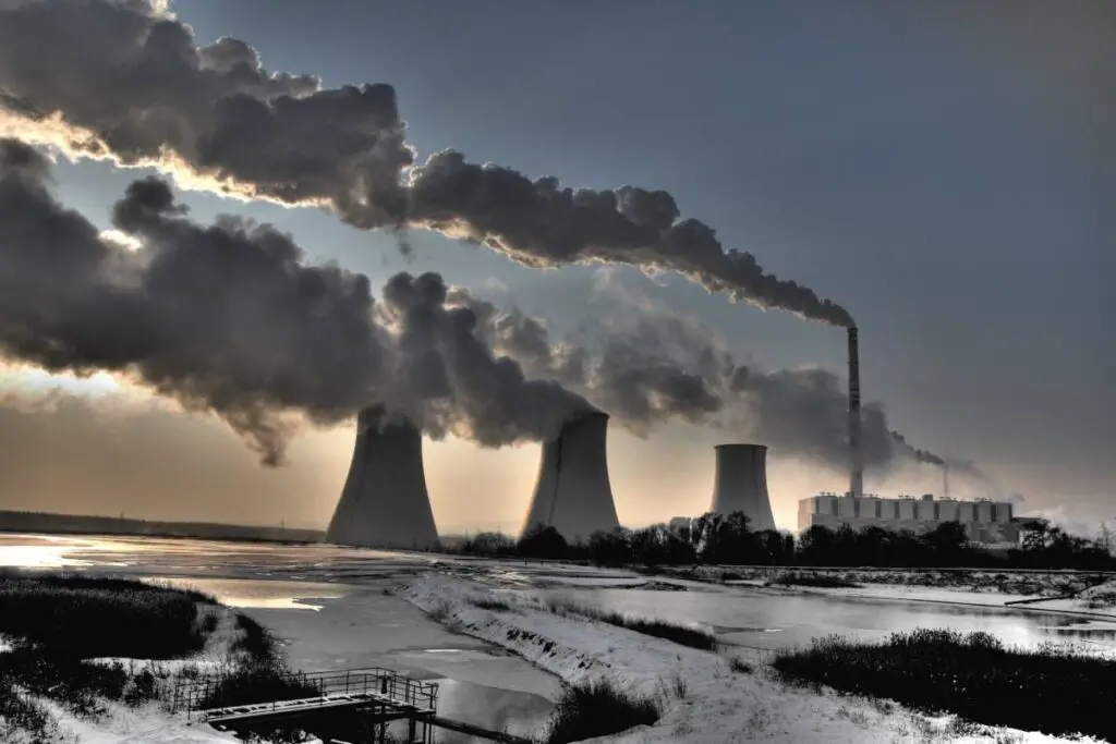 Coal powerplant against sun with several chimneys and fumes