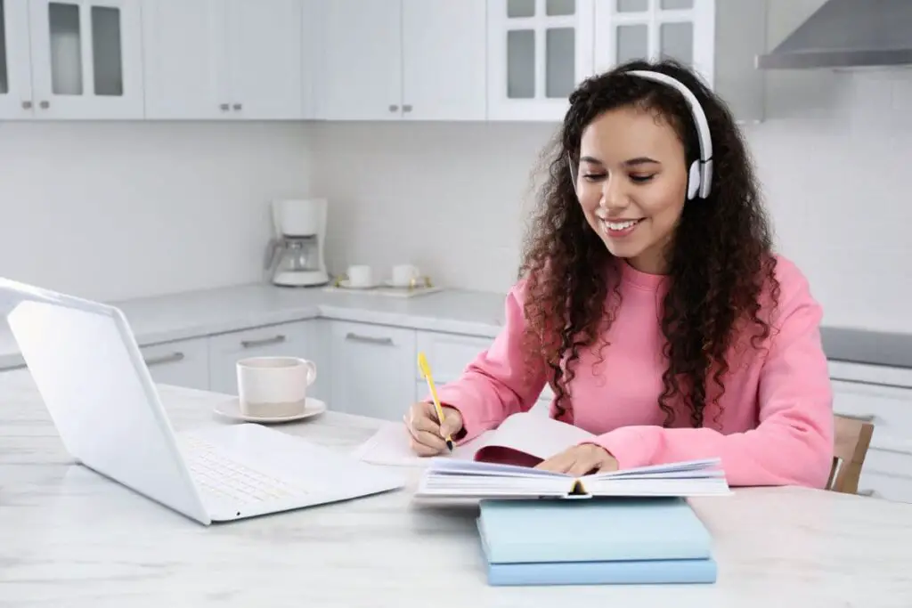 African American woman with modern laptop listening to best music studying in kitchen