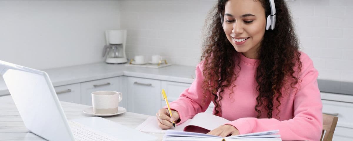 African American woman with modern laptop and headphones studying in kitchen