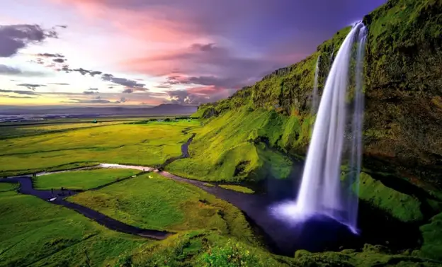 The meaning of nature depicted in a beautiful waterfallling into a river meandering across acres of greenfields. (Image source: https://www.naturaluniversalsecrets.com/blog/what-does-the-natural-world-include-top-10-list/)