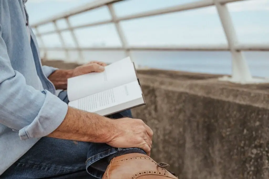 man sitting on sea front, reading a book