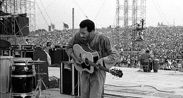 Richie Havens photographed on stage with crowd in the background in black and white - https://www.celebstoner.com/high-tunes/rock/2013/04/22/richie-havens-freedom/