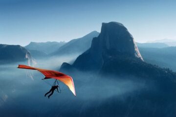 photo of hang glider with orange sail and blue mountain background