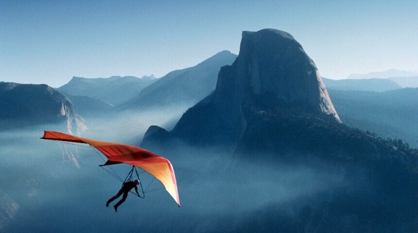 photo of hang glider with orange sail and blue mountain background