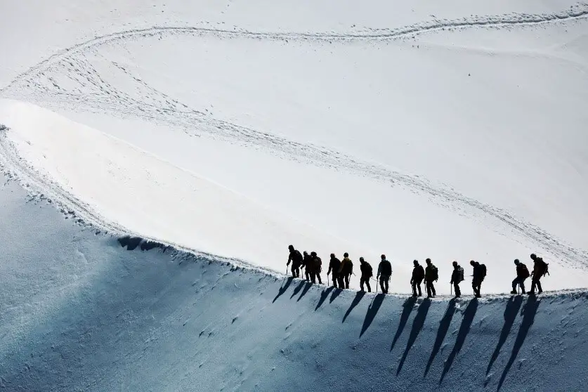 13 mountaineers walking along a snow covered ridge