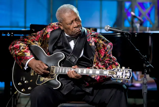 BB King playing a guitar sitting in a colourful jacket