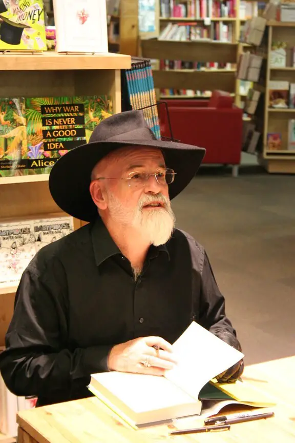 Photo of Sir Terry Pratchett in a black Homburg hat signing books