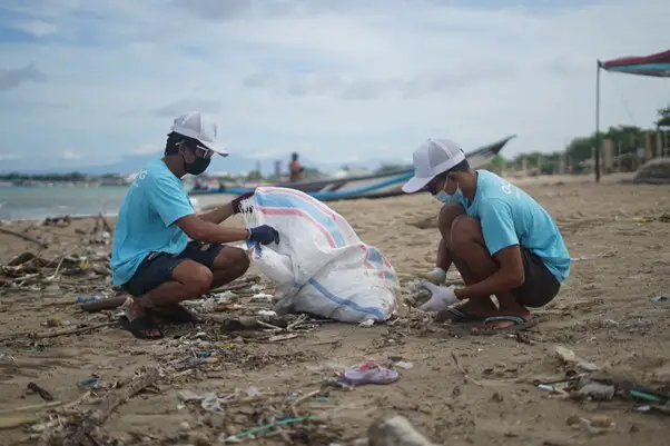 Two Indonesian men clean the beach on behalf of Ocean Cleanup Group.