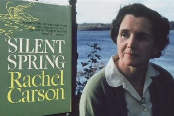 Photo of Rachel Carson sat by a lake looking at her book placard