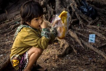 young cambodian child on his haunches guarding a baguette