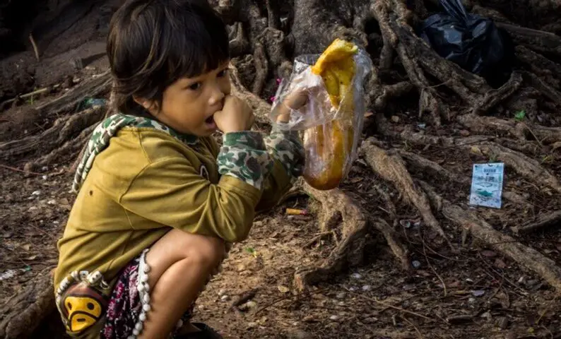 young cambodian child on his haunches guarding a baguette